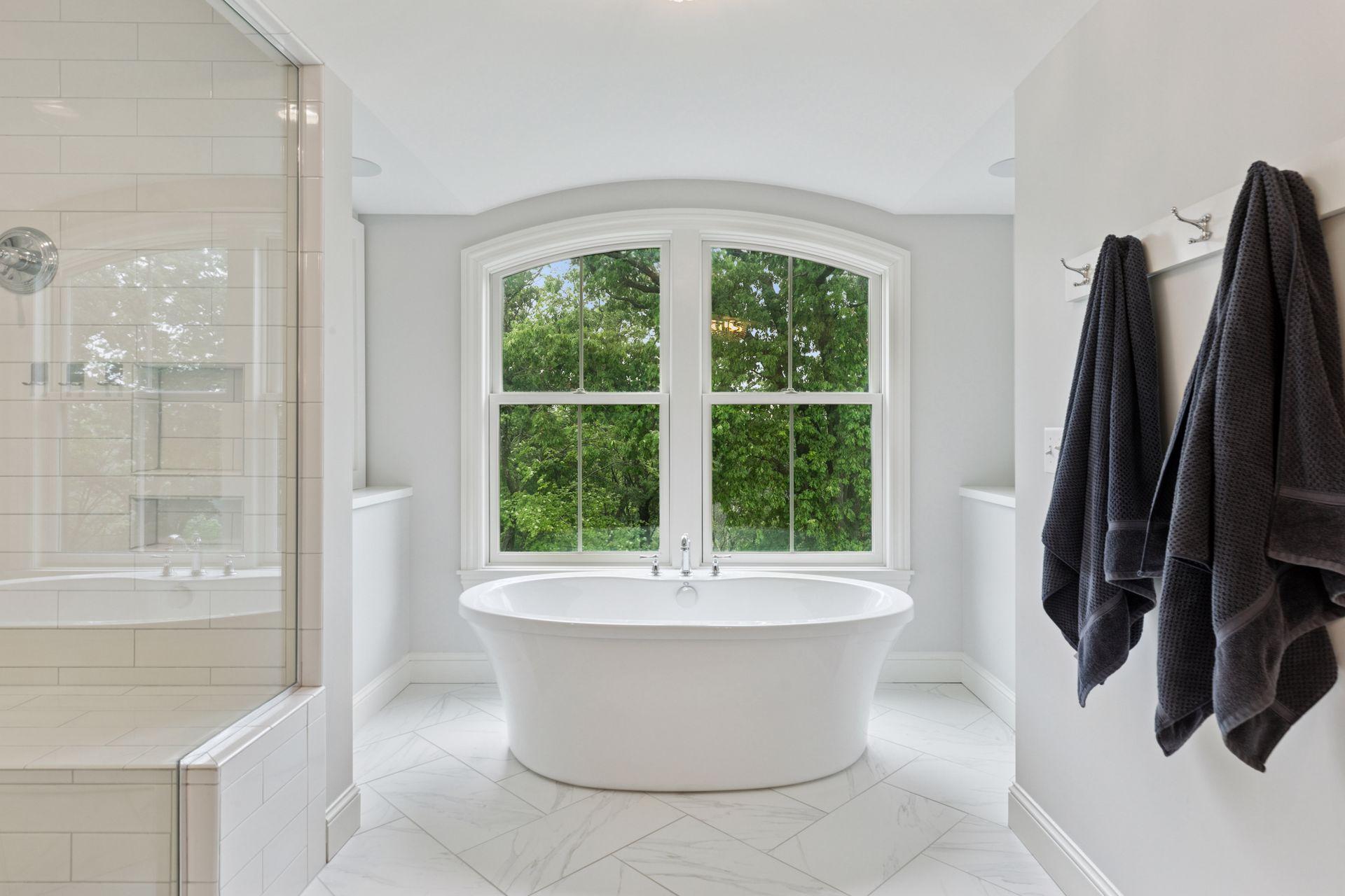 Enjoy a spa-like experience with the oversized glass shower, soaking tub, and bright natural light pouring in through expansive windows.