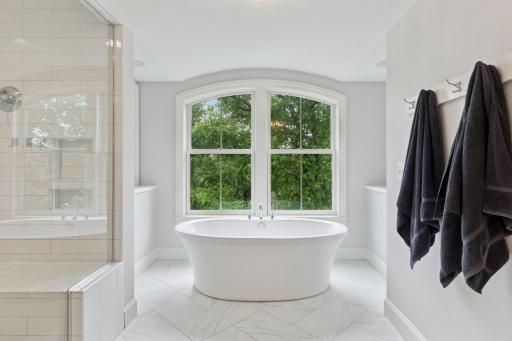 Enjoy a spa-like experience with the oversized glass shower, soaking tub, and bright natural light pouring in through expansive windows.