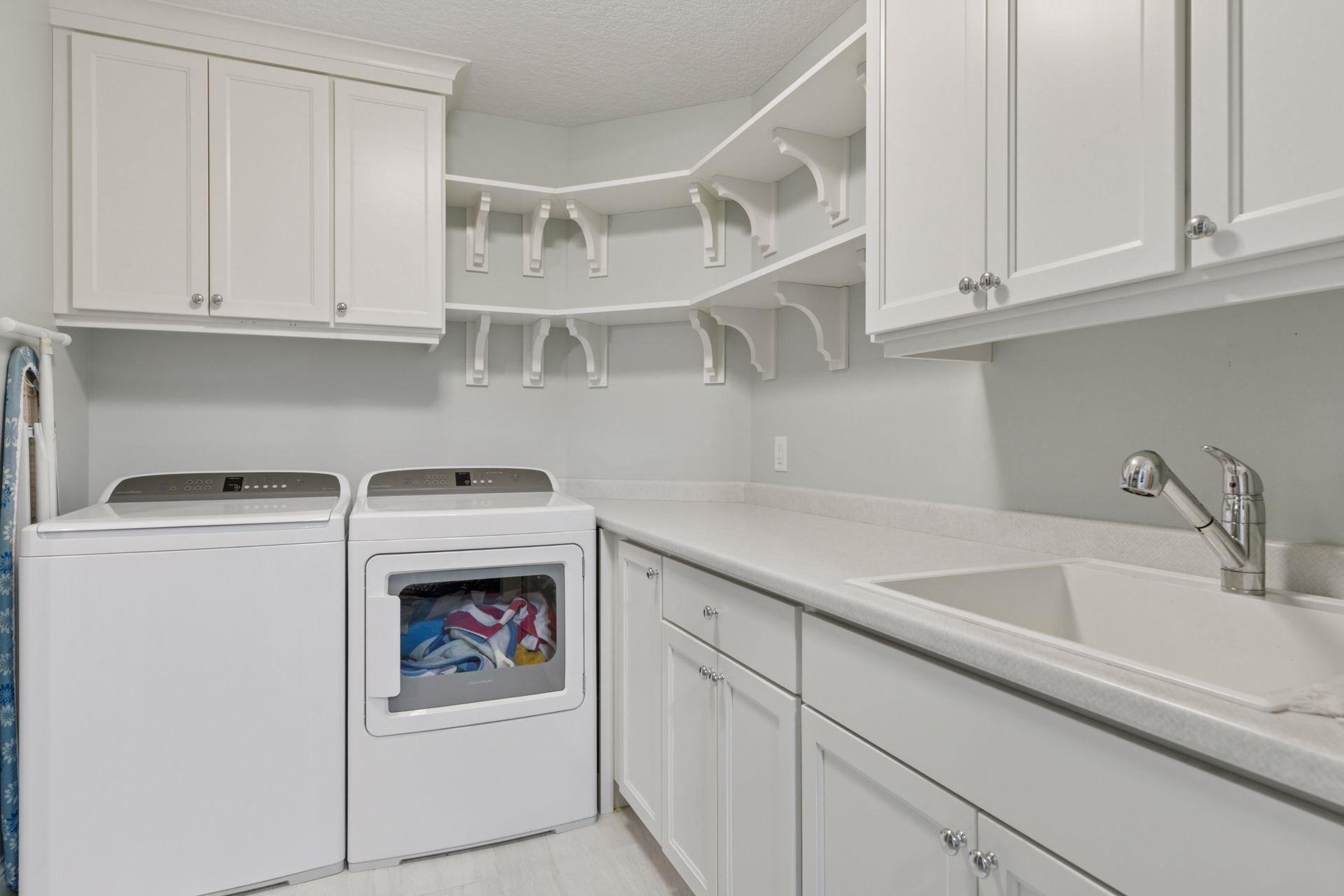 Bright and functional laundry room with washer, dryer, deep utility sink, and ample cabinet storage, conveniently connected to the owner's walk-in closet and upper main hallway.