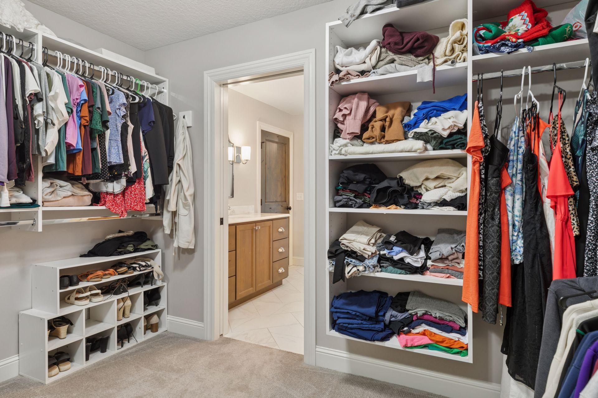 Custom closet layout with organized shoe storage, open shelving, and access to the primary ensuite bathroom.