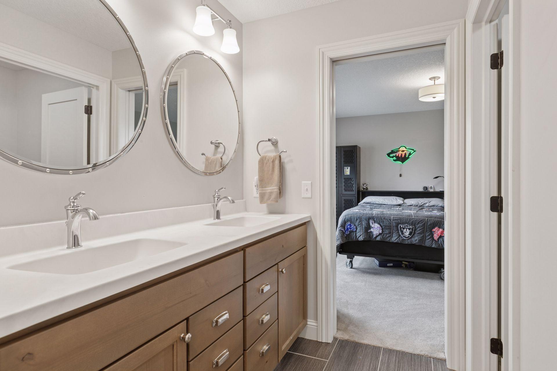 Bathroom with dual sinks, wood cabinetry, and stylish round mirrors connecting to an upper bedroom.