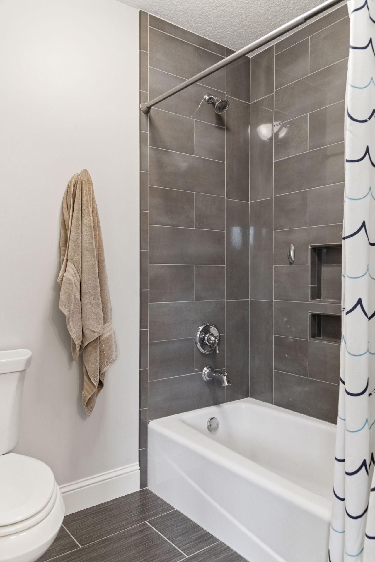 Modern tiled bathtub and shower combo featuring large-format gray tiles and built-in niche shelving.