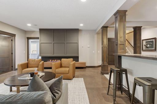 Alternate view of the lower-level living area showcasing the cozy seating arrangement, fireplace, and open-concept bar area.