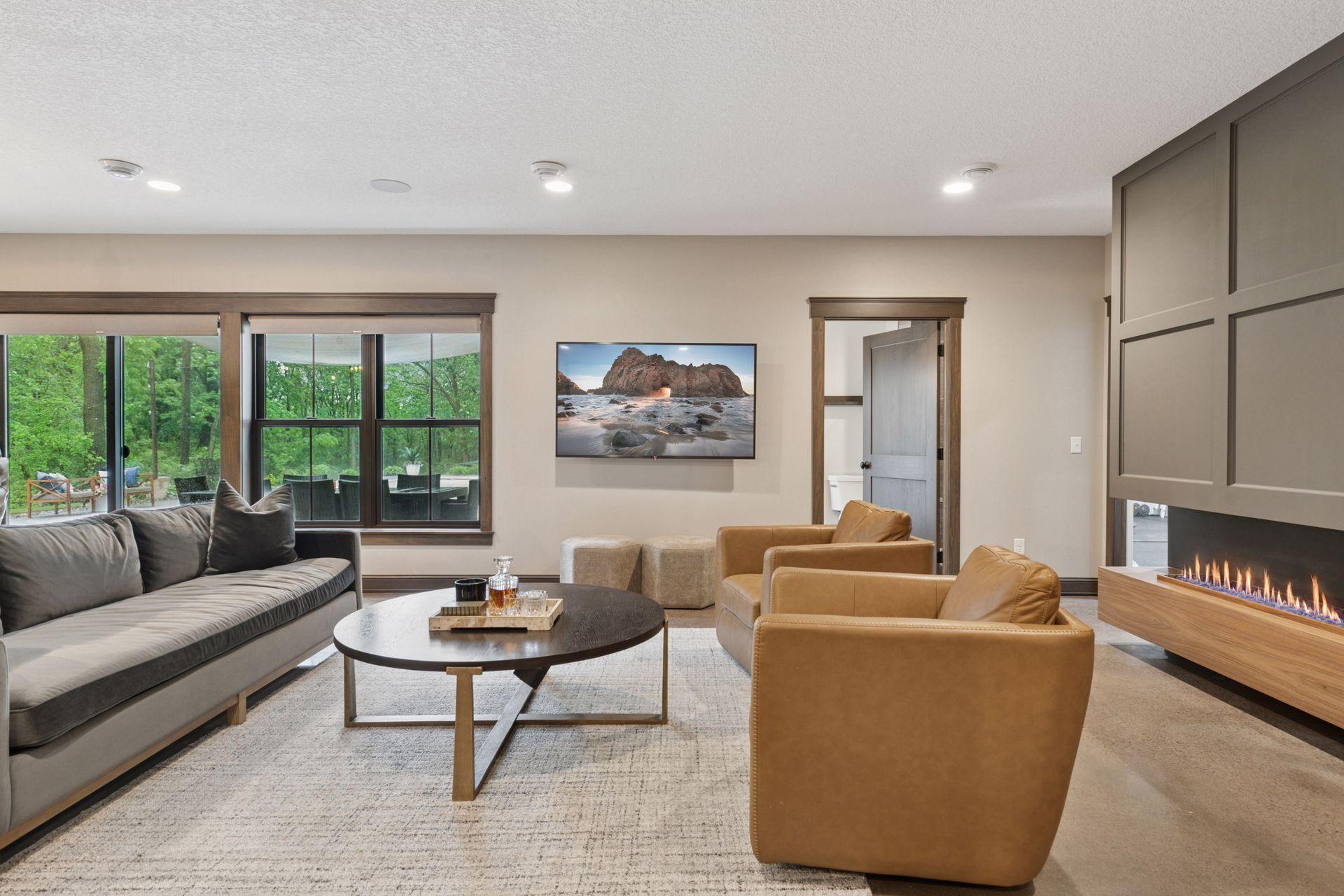 Lower-level family room with wall-mounted TV, direct walkout access to the patio, and beautiful natural light through oversized windows.