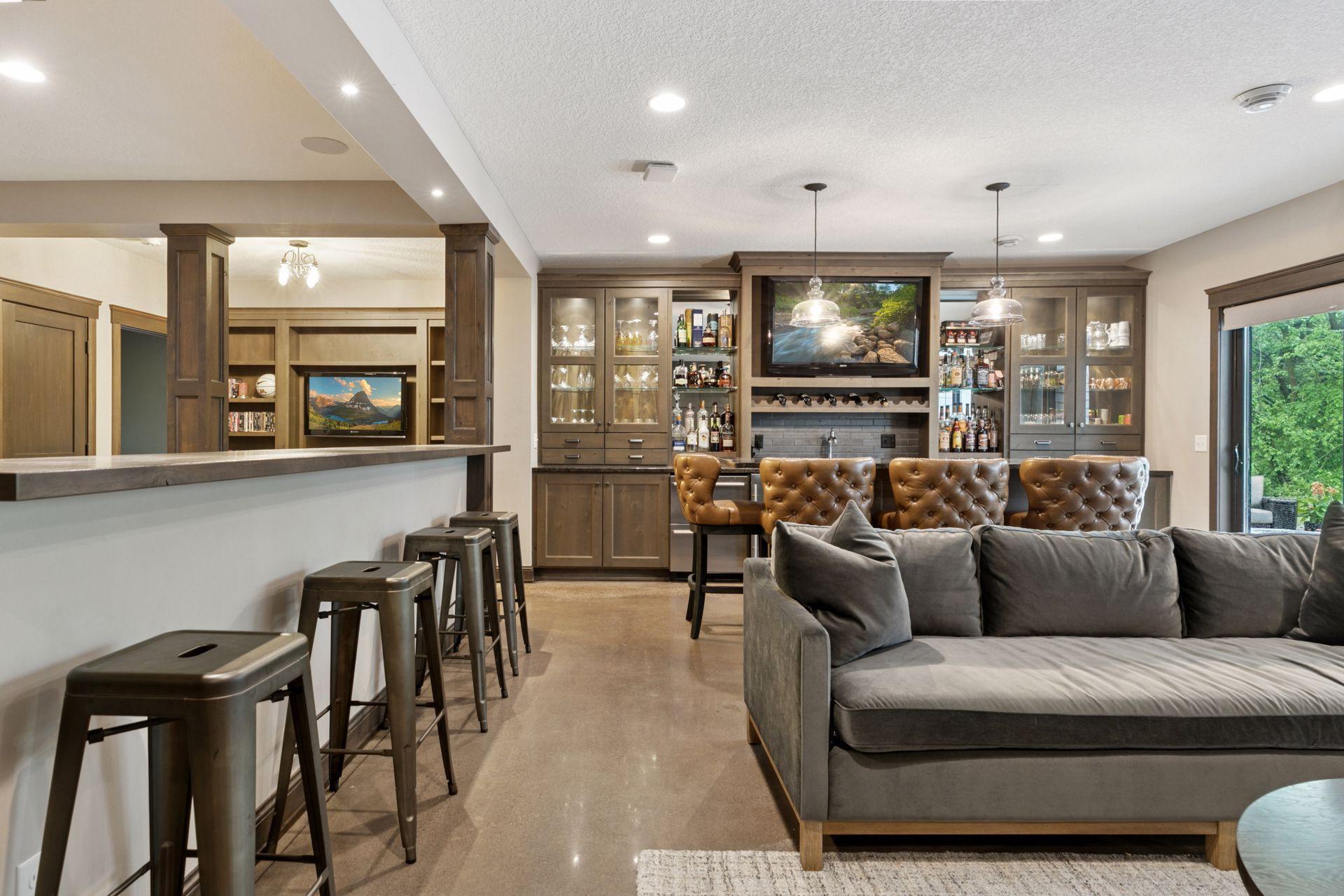 Expansive lower-level lounge featuring a custom bar, large windows, and a wall-mounted flat screen for effortless entertaining.