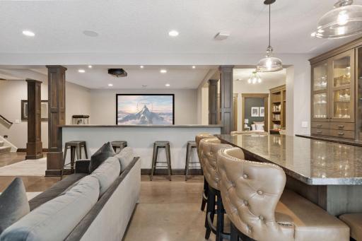Luxurious bar setup with tufted leather stools, illuminated glass cabinets, and built-in wine and liquor storage.