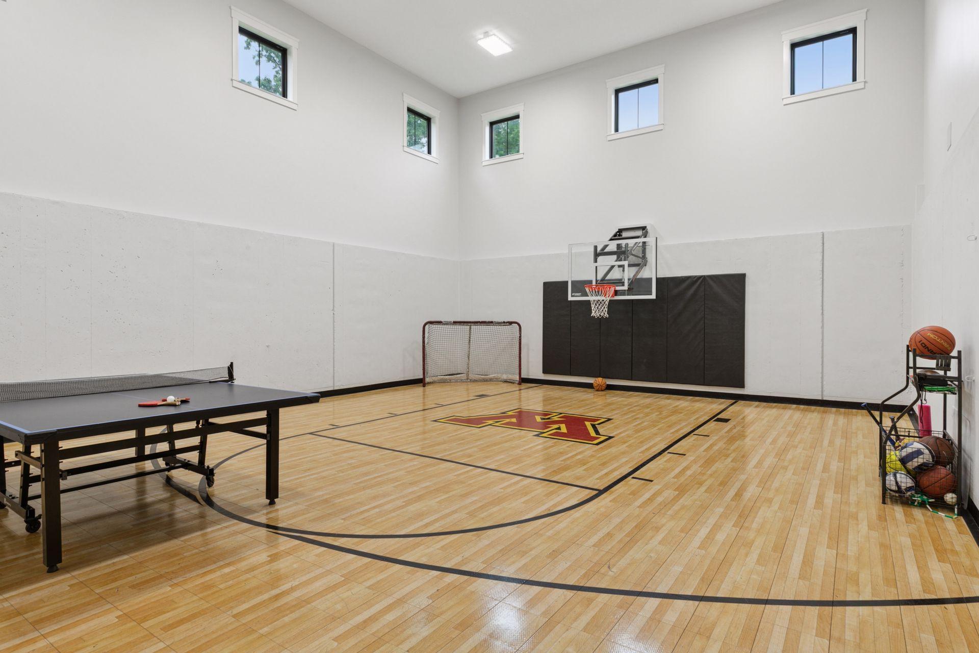 Versatile indoor sport court with hardwood flooring, basketball hoop, hockey net, and space for ping pong—perfect for year-round fitness and family fun.