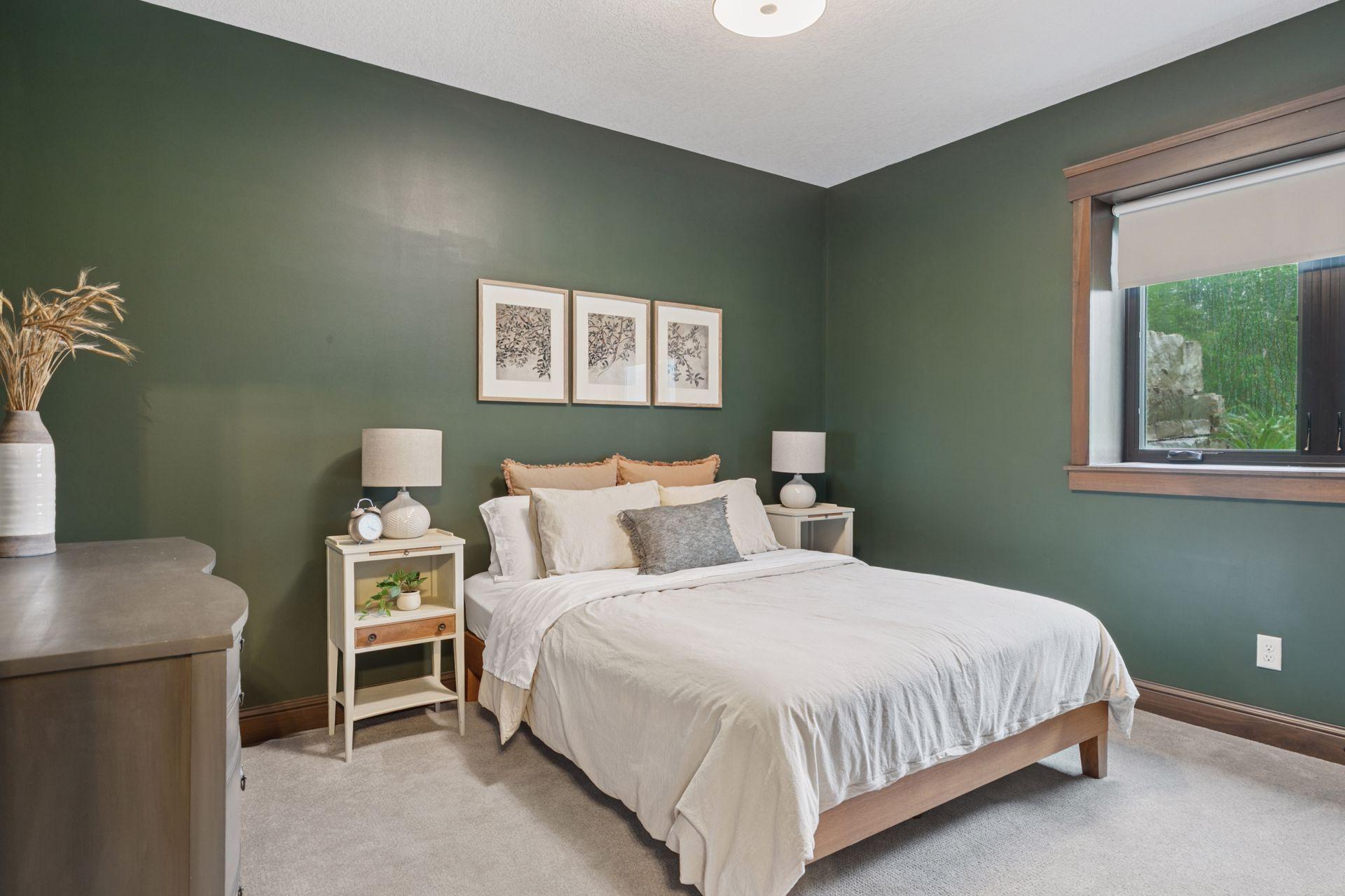 Tranquil lower-level bedroom with deep green accent walls, soft carpeting, natural light, and warm wood trim—ideal for guests or multi-generational living.