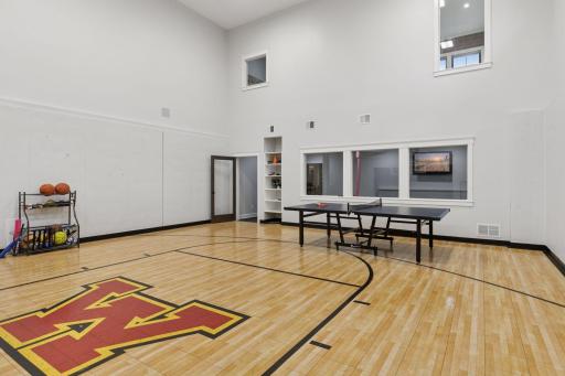 Light-filled sport court with basketball and ping pong setups, high ceilings, custom flooring, and direct views into the adjacent home gymâperfect for family fun and training.