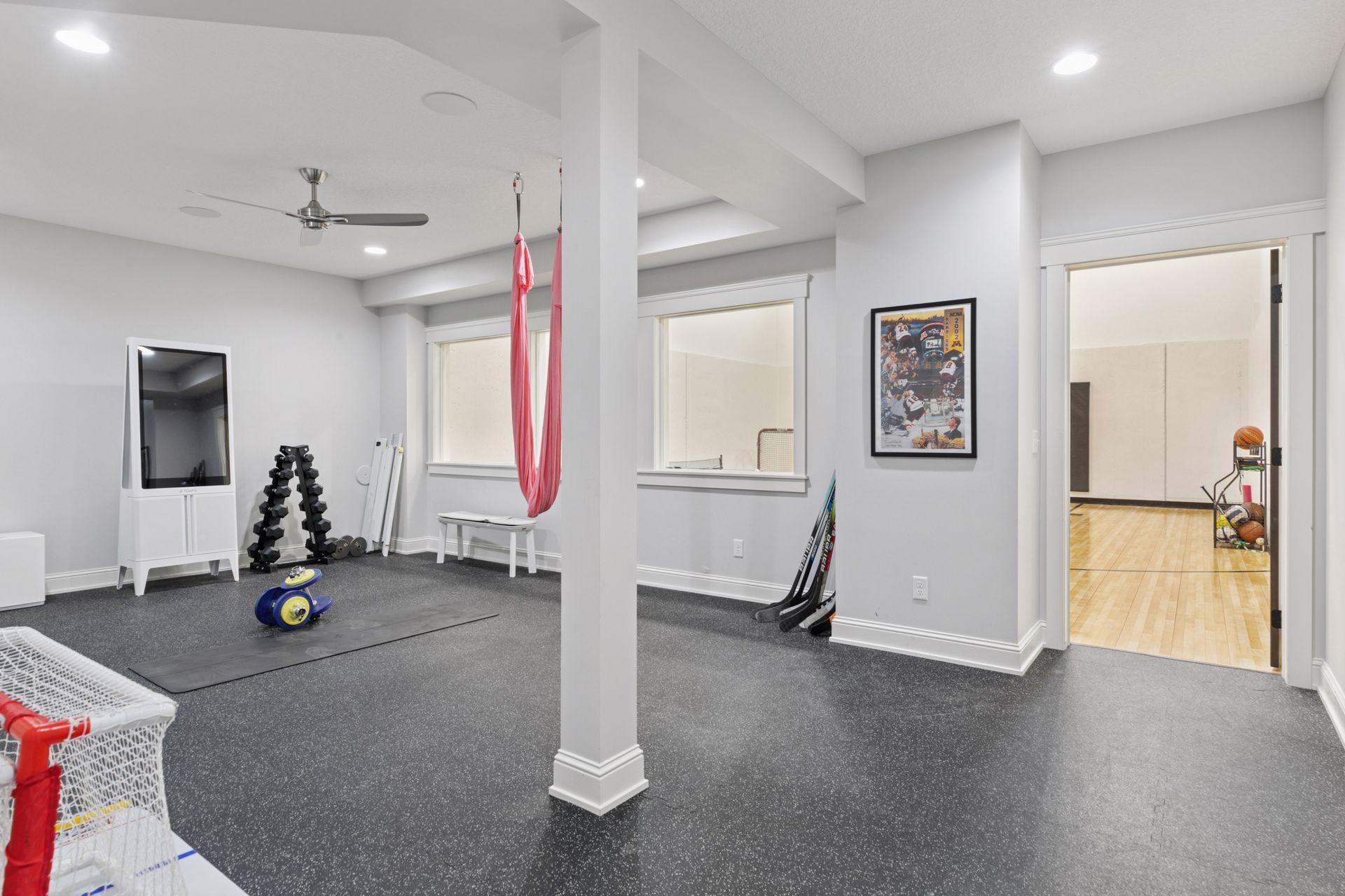 Spacious home gym with rubber flooring, natural light, ceiling fan, and adjacent indoor sport court—perfect for workouts, training, and year-round recreation.