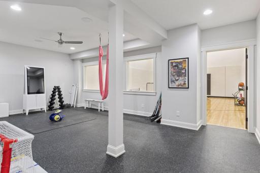 Spacious home gym with rubber flooring, natural light, ceiling fan, and adjacent indoor sport courtâperfect for workouts, training, and year-round recreation.