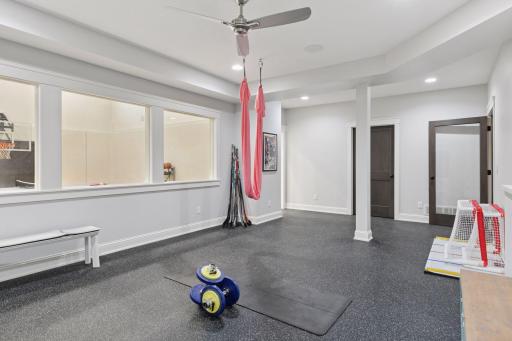 Expansive home gym with sport court views, rubber flooring, ceiling fan, and flexible space for yoga, weight training, and kidsâ activitiesâdesigned for all-around wellness.