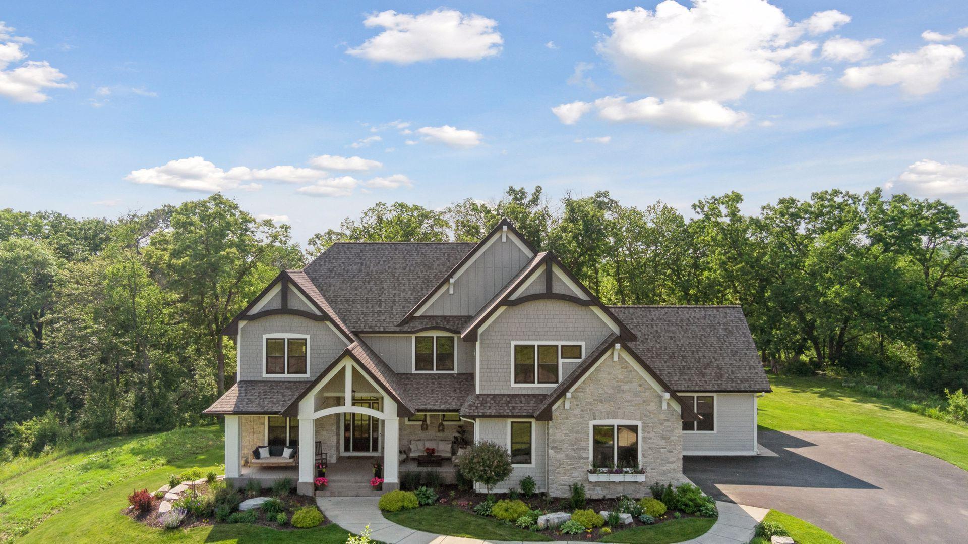 Stunning custom home nestled on a private, wooded lot with lush landscaping, elegant stone façade, and charming covered front porch—offering curb appeal and serene surroundings.
