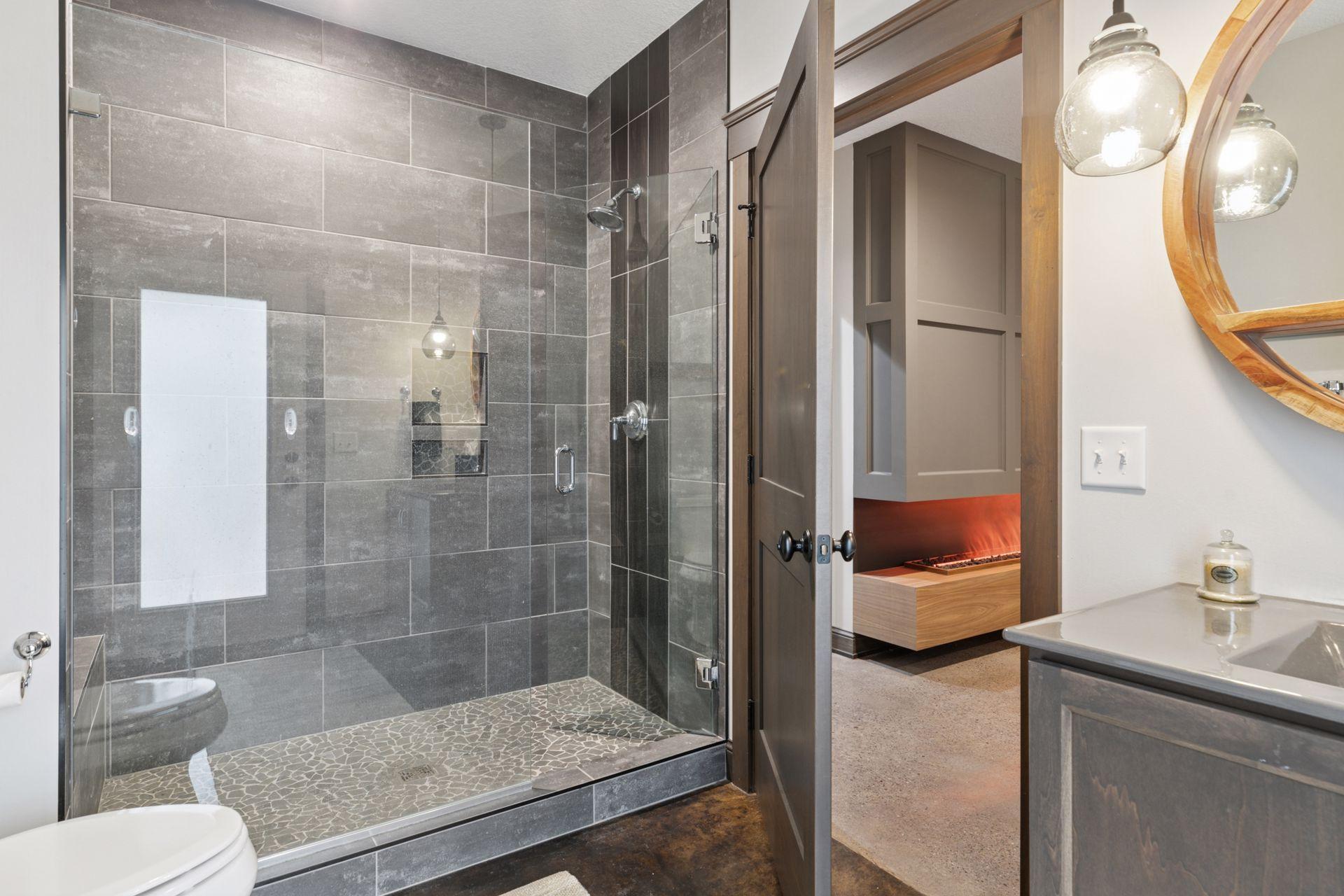 Chic lower-level bathroom with walk-in tiled shower, stone floor detail, stylish vanity, urinal, and direct access to living and pool areas—perfect for guests and poolside use.