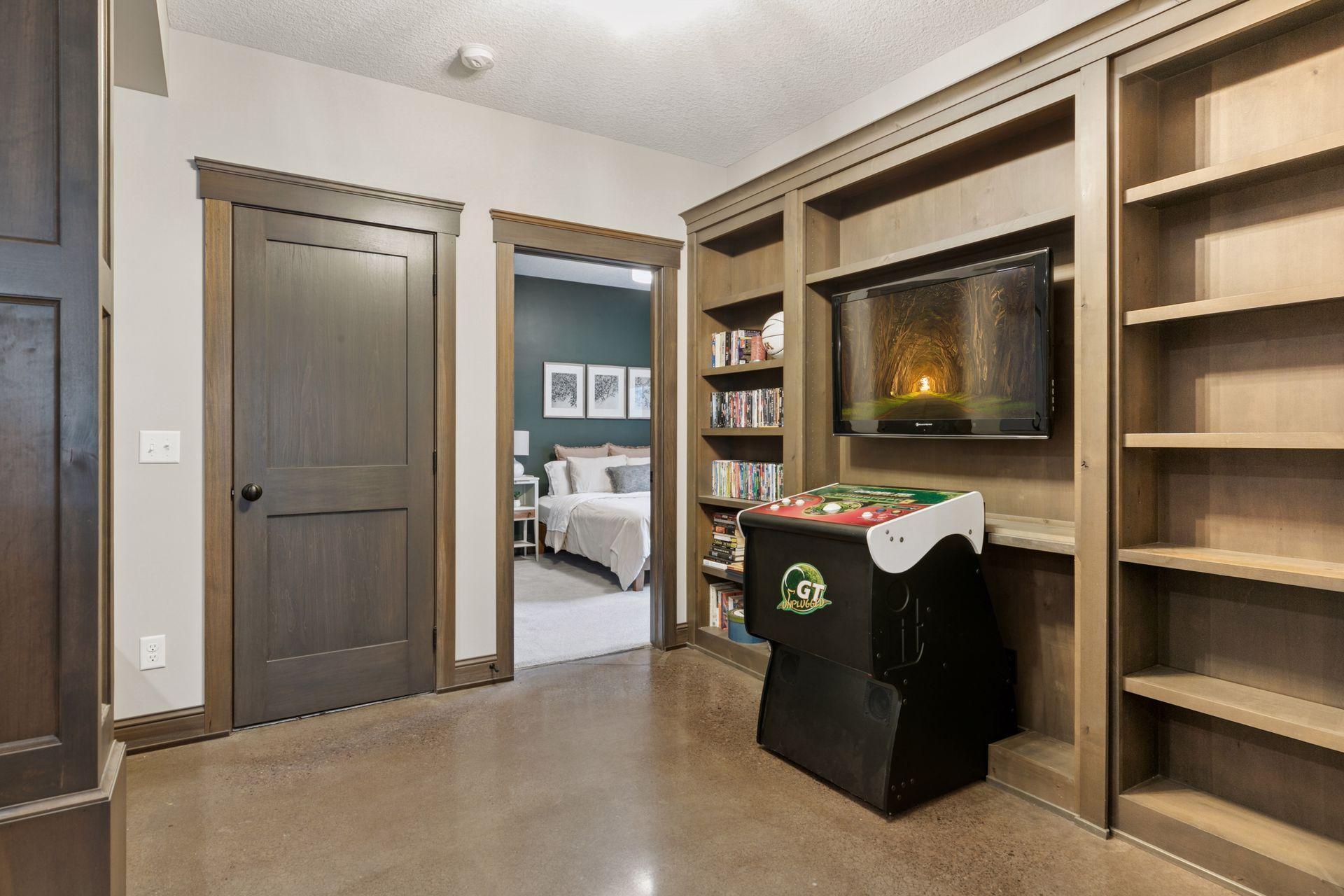 Cozy entertainment nook with built-in shelving, arcade game, wall-mounted TV, and polished concrete floors—perfect for movie nights or gaming just steps from the guest suite.