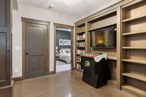 Cozy entertainment nook with built-in shelving, arcade game, wall-mounted TV, and polished concrete floorsâperfect for movie nights or gaming just steps from the guest suite.