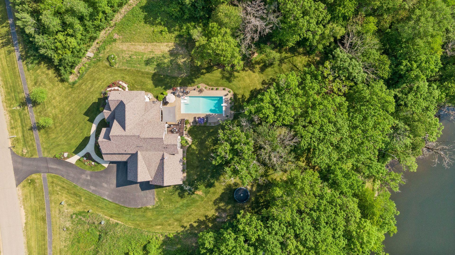 Overhead view reveals a beautifully landscaped backyard oasis with an in-ground pool, spacious patio, and wooded privacy—just steps from a peaceful water’s edge.