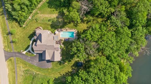 Overhead view reveals a beautifully landscaped backyard oasis with an in-ground pool, spacious patio, and wooded privacyâjust steps from a peaceful waterâs edge.