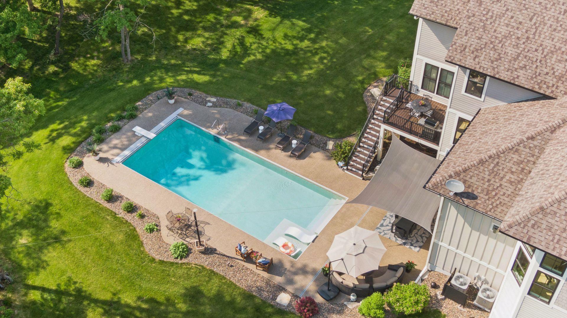 Stunning backyard retreat with an in-ground pool, sun shelf, lounging areas, and patio dining—perfect for entertaining or unwinding in a peaceful, tree-lined setting.