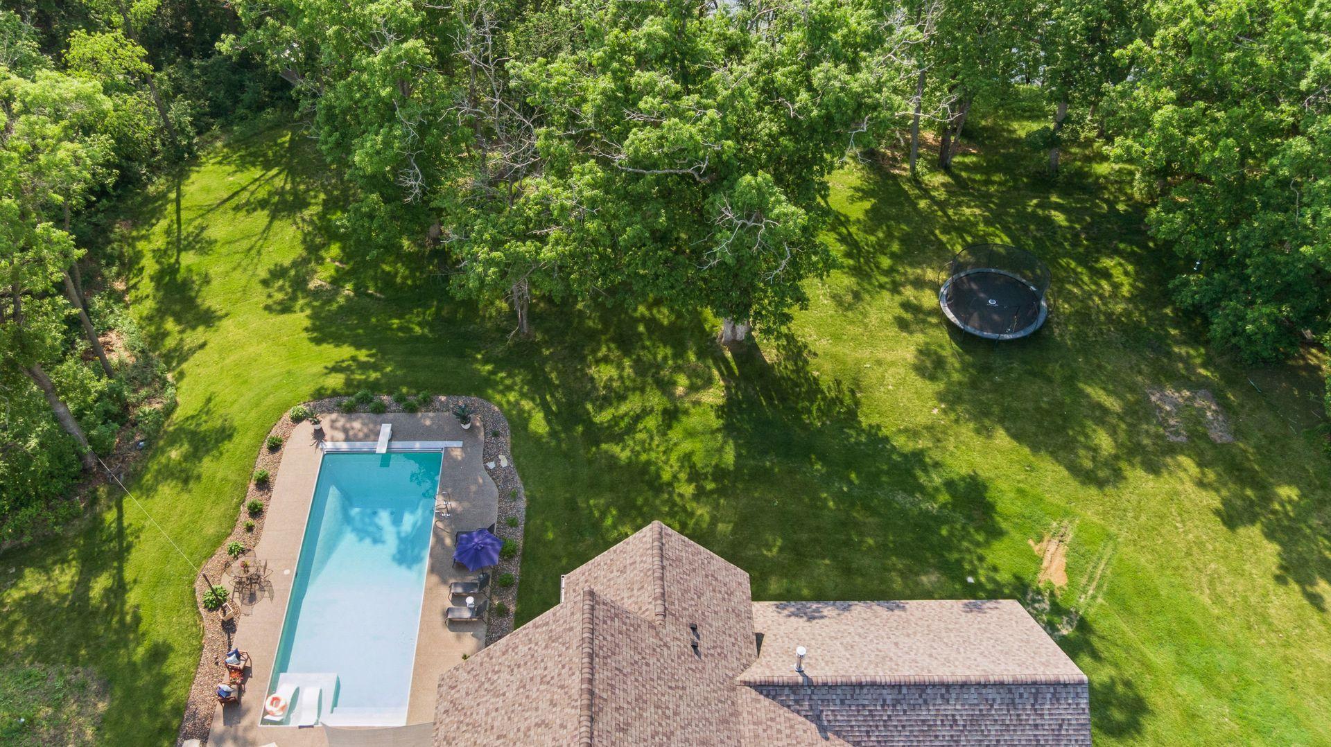 Bird’s-eye view of the expansive backyard featuring a pristine pool, lush lawn, trampoline, and mature tree canopy—ideal for recreation and relaxation in total privacy.