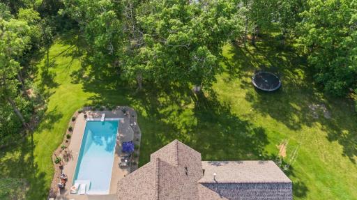 Birdâs-eye view of the expansive backyard featuring a pristine pool, lush lawn, trampoline, and mature tree canopyâideal for recreation and relaxation in total privacy.