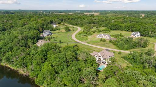 Expansive aerial view showcasing this secluded, wooded property with pool and water frontageâtucked into a high-end neighborhood with rolling hills and estate-style homes.