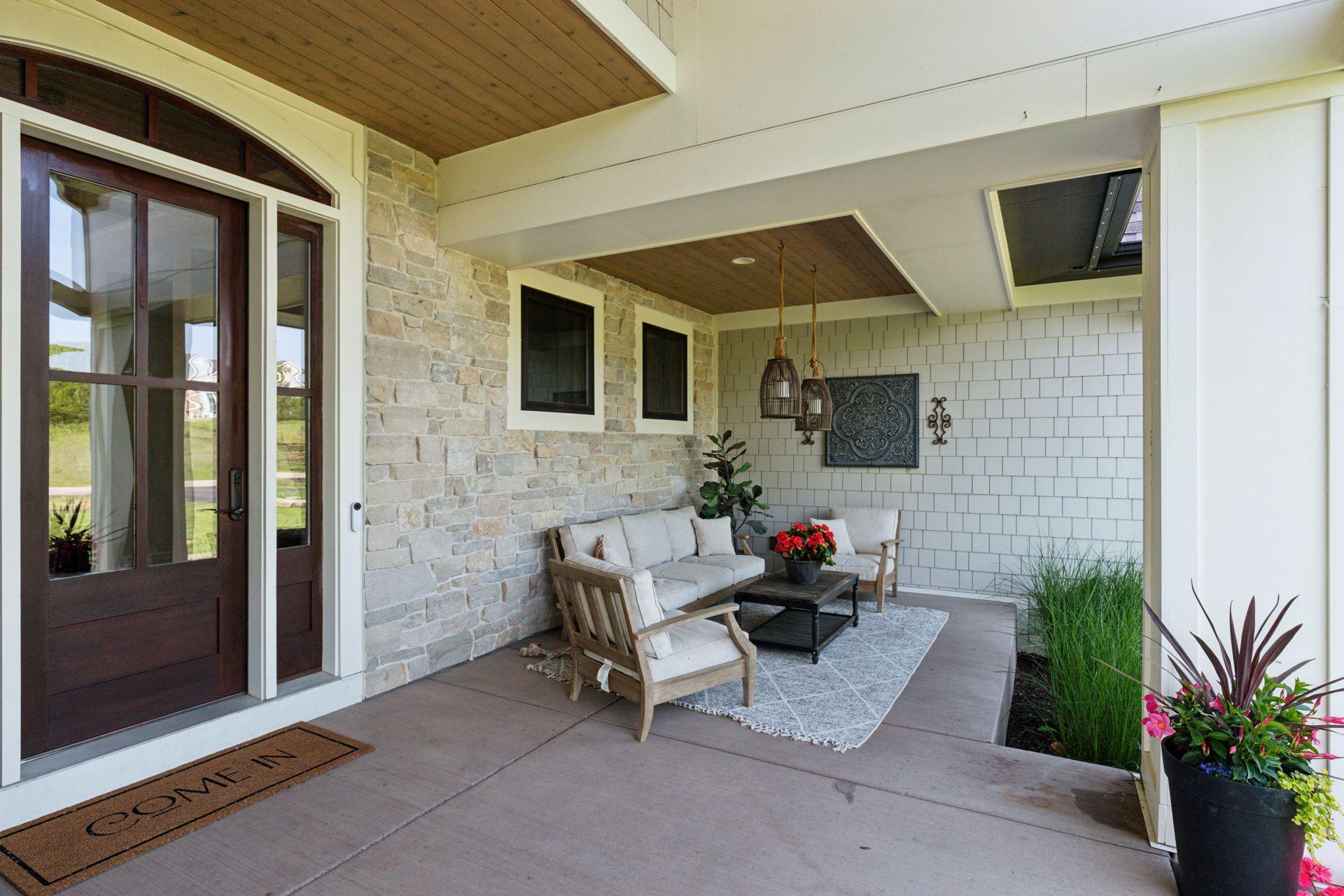Chic and cozy front porch seating area with stone wall, ceiling detail, and elegant lighting—ideal for casual entertaining.