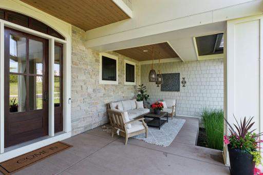 Chic and cozy front porch seating area with stone wall, ceiling detail, and elegant lightingâideal for casual entertaining.