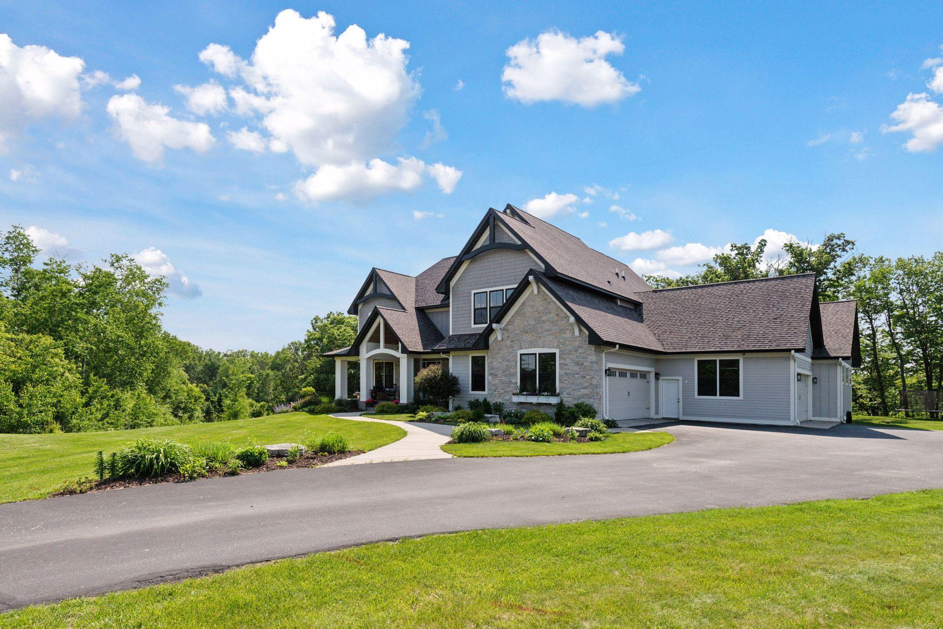 Curved driveway approach highlighting the grand facade, lush yard, and idyllic wooded surroundings.