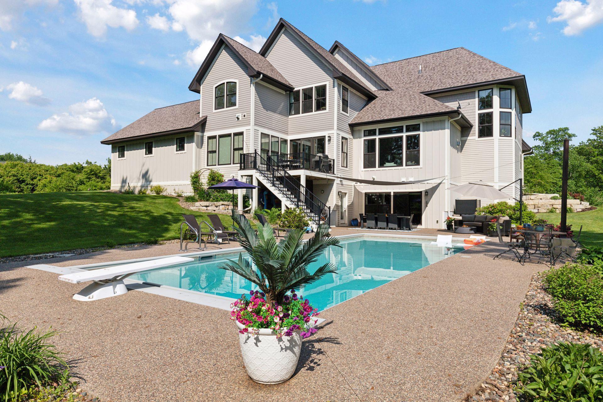 Immaculate poolside retreat with lush landscaping, diving board, and ample seating. Beautiful architectural lines frame the home, offering seamless indoor-outdoor living.