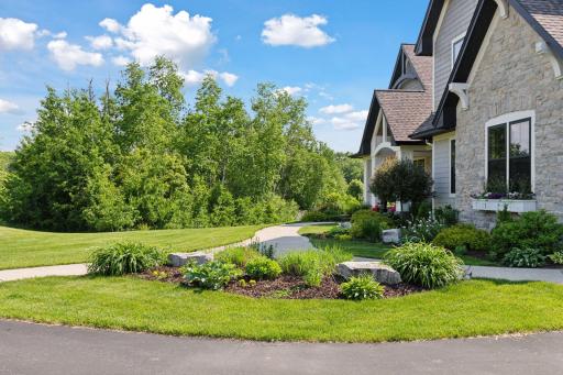 Vibrant landscaping frames the walkway with stone accents, perennials, and seasonal bloomsâlush and low-maintenance.