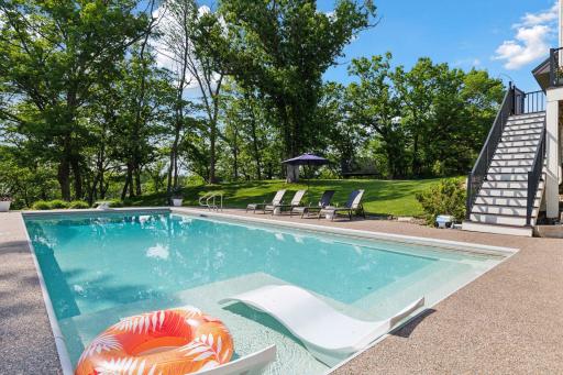 Peaceful poolside setting with partial shade, lush greenery, and clean design. Includes integrated shallow lounging shelf and steps for easy entryâan entertainerâs dream.