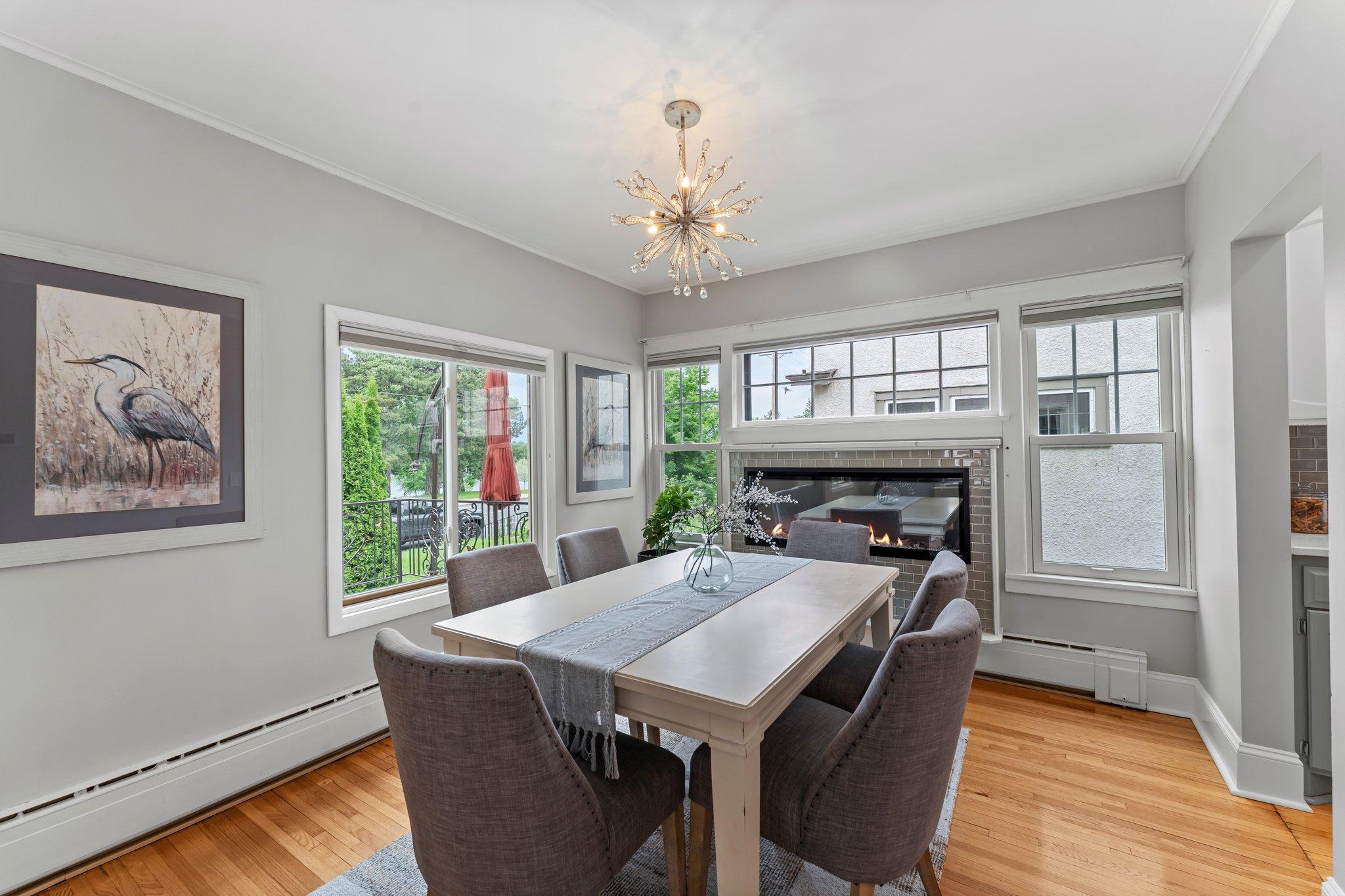 The adjoining dining room features a stylish electric fireplace with a tiled surround and a statement light fixture, offering a perfect setting for gatherings or quiet dinners.