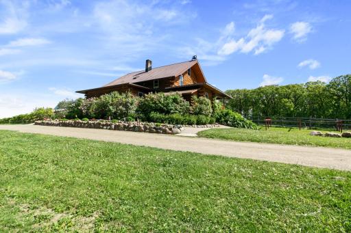 View of the North side of the house, showing lilac bushes, rock wall, flower beds, sidewalk and driveway. The large dinner bell on the top of the house will be severed from the sale, as it is a family heirloom. The smaller one will remain.