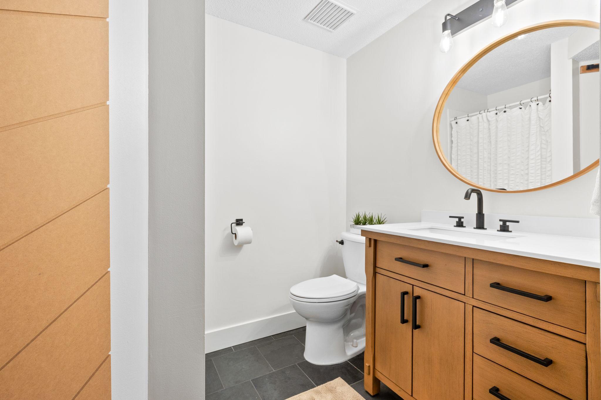 Lower level 3/4 bathroom with tiled floors, wood vanity, toilet, and custom closet doors.