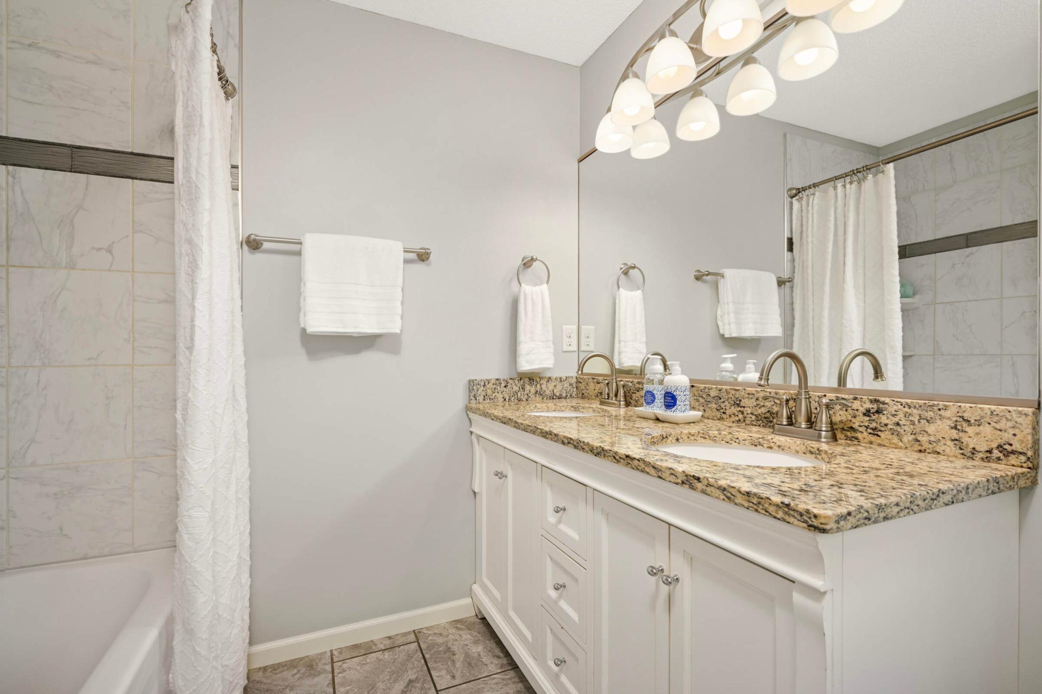 The updated primary bathroom features a granite-topped dual vanity, brushed nickel fixtures, and tiled bathtub surround with modern accents.