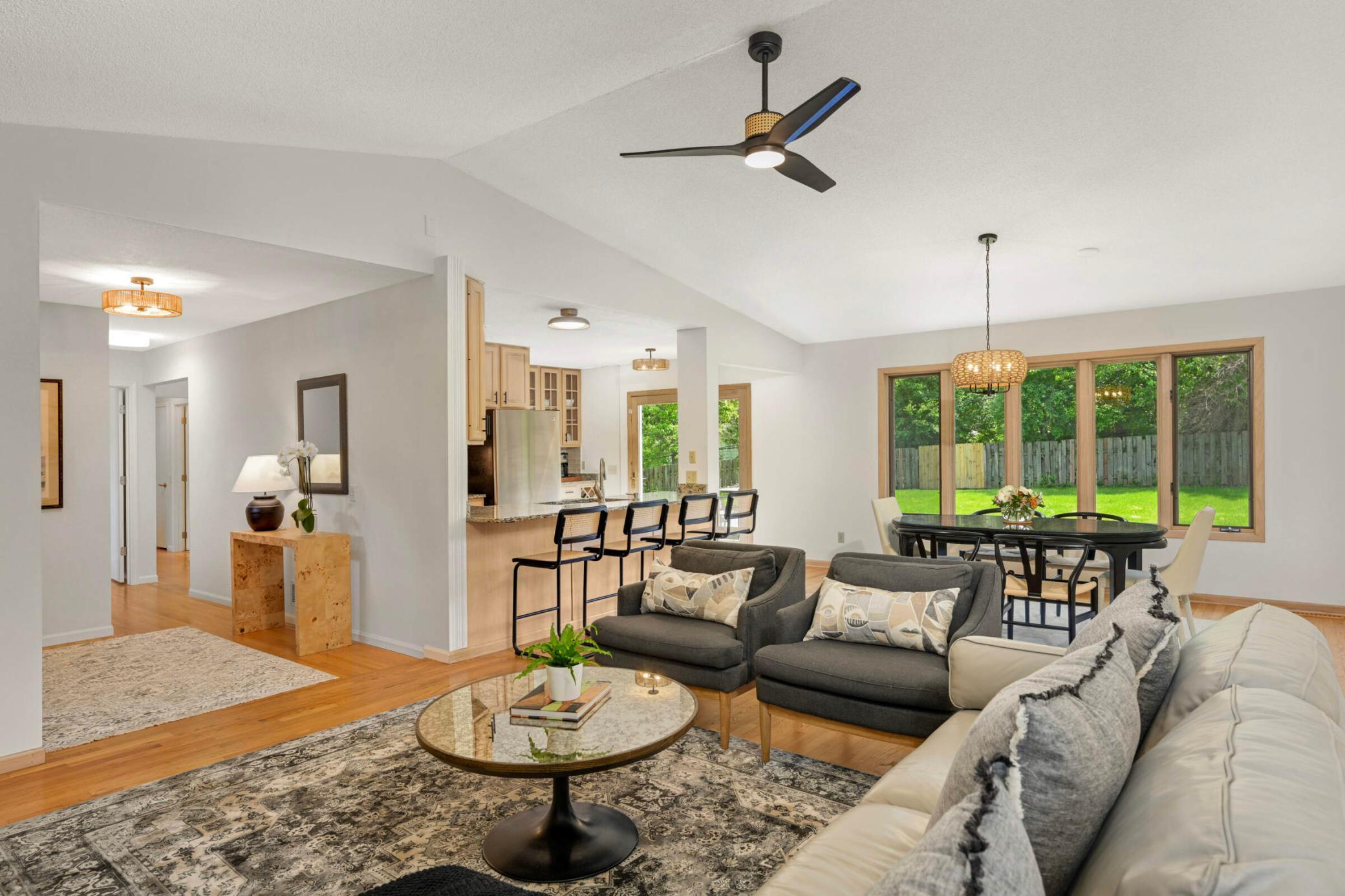 Bright and open-concept living space features vaulted ceilings, a spacious dining area, a breakfast bar, and large windows overlooking the private backyard.
