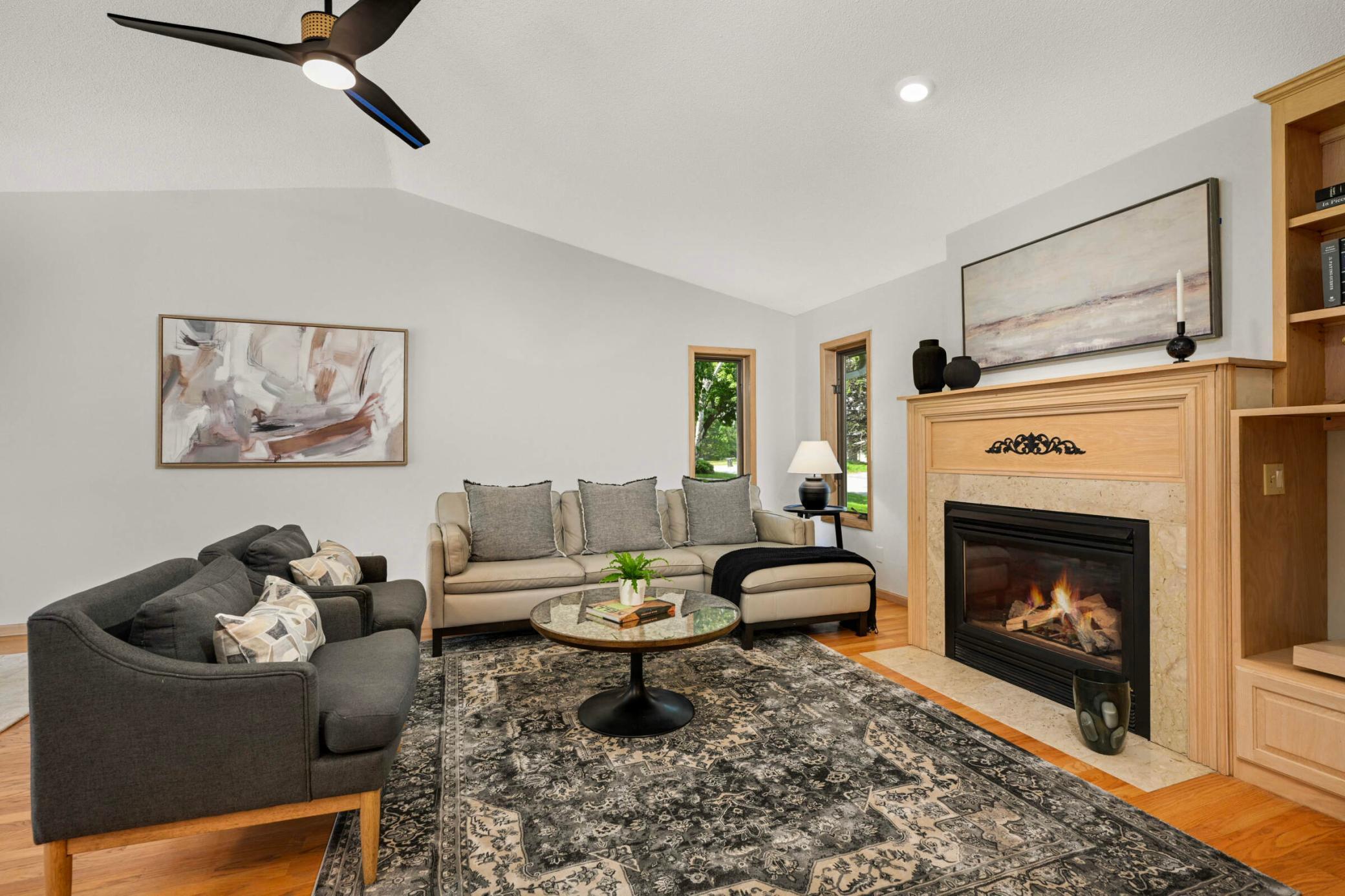 The inviting living room boasts vaulted ceilings, a cozy gas fireplace, abundant natural light, and elegant wood accents for a warm and stylish ambiance.