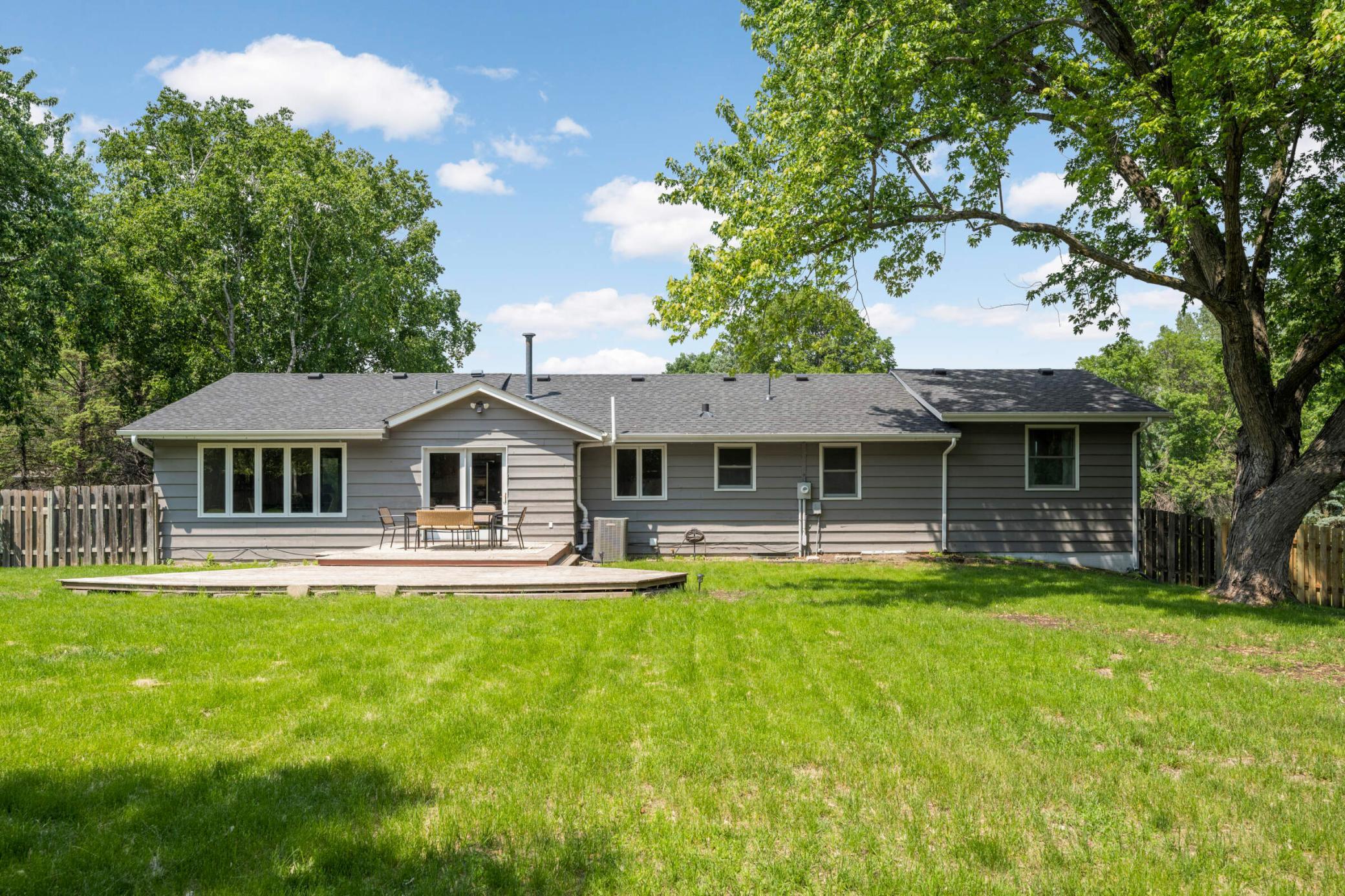 Spacious fenced backyard with large deck and mature trees, perfect for outdoor entertaining and relaxation.