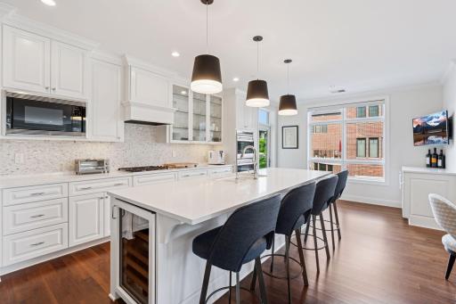Kitchen features a large center island with built-in wine refrigerator, gas cooktop, double wall ovens, walk-in pantry, and access to a small grilling balcony