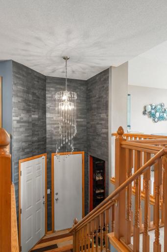 As you enter the home, you're welcomed by a charming foyer featuring soaring 14-foot ceilings, a striking custom hanging light fixture, stone-accented walls, and a convenient entry closet with shelving—perfect for storing shoes and jackets.