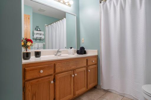 The primary bedroom’s full bathroom is also accessible from the hallway for added convenience. It features tile flooring, a single vanity, a built-in linen cabinet, and a tub/shower combination.
