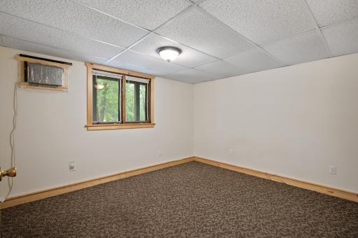 The third bedroom on the lower level features neutral tones and a lookout window with views of mature trees and surrounding nature.