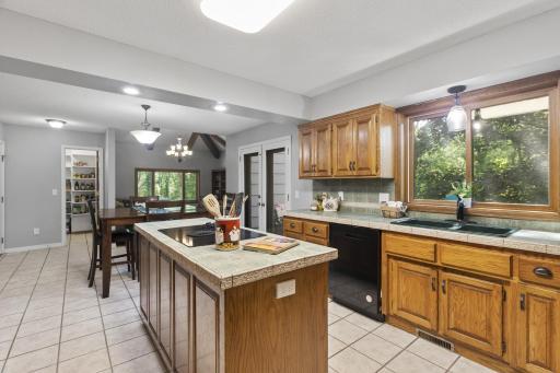 Chef’s kitchen featuring custom cabinetry, center island with cooktop, double ovens, ceramic tile floors, counters, and backsplash. Enjoy new/newer stainless steel appliances, a large window, and a fully enclosed walk-in pantry.