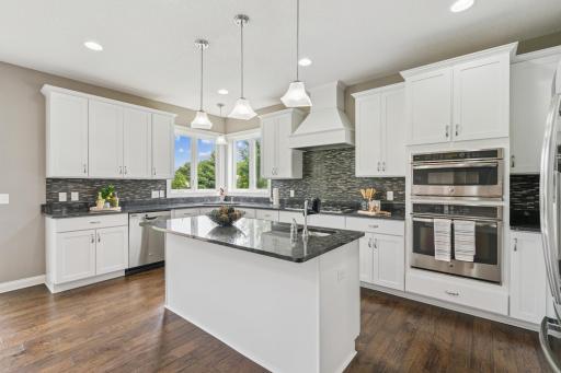 This gourmet kitchen features white cabinetry, granite countertops, double ovens, a center island, and expansive windows that flood the space with natural light.