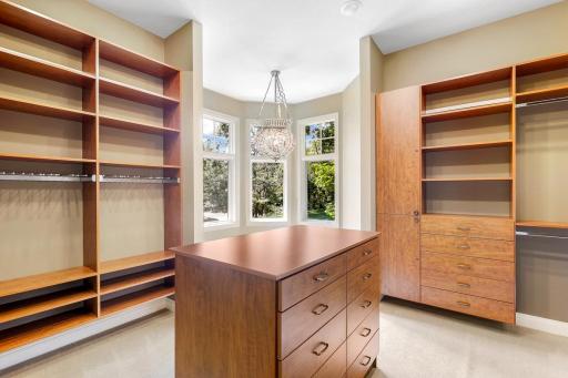 The ensuite walk-in closet boasts ample overhead lighting, natural light from a bank of windows, custom shelving and hanging racks throughout. It connects through to the main-floor laundry room for easy access, and for quiet exits.