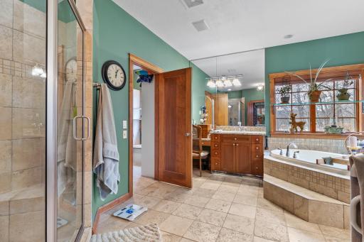 Primary bath with custom tile flooring and custom tile shower. Large tub with jets. Two separate sink areas and dressing table. Entry to second primary walk-in closet shown.