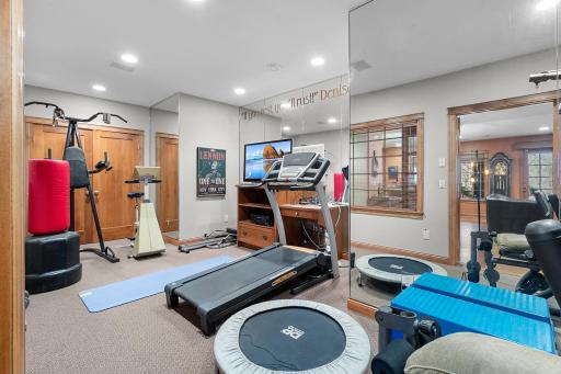 Lower-level exercise room with space for several machines and weights. Mirrored walls and French, windowed doors to lower-level hallway. Ceiling speakers connect to media cabinet. Exercise equipment included.