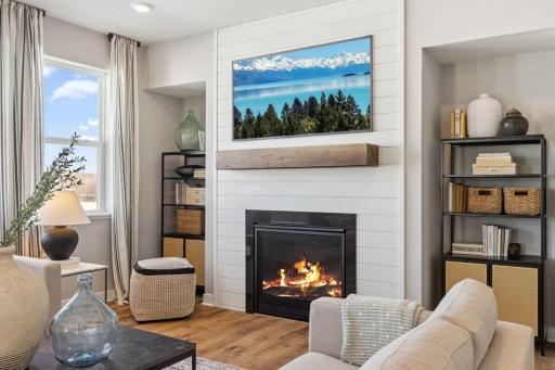 The family room is punctuated by a gas fireplace - which serves as a cozy bookend to the area and highlights a space that's flooded in natural light via these four soaring windows! Photo of a model home, color & options will vary.