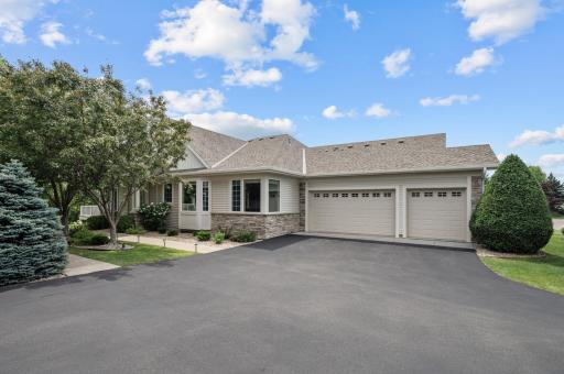 A sunny angle on the front entrance and garage area, highlighting the attractive mix of siding and stonework, mature landscaping, and a wide asphalt driveway.